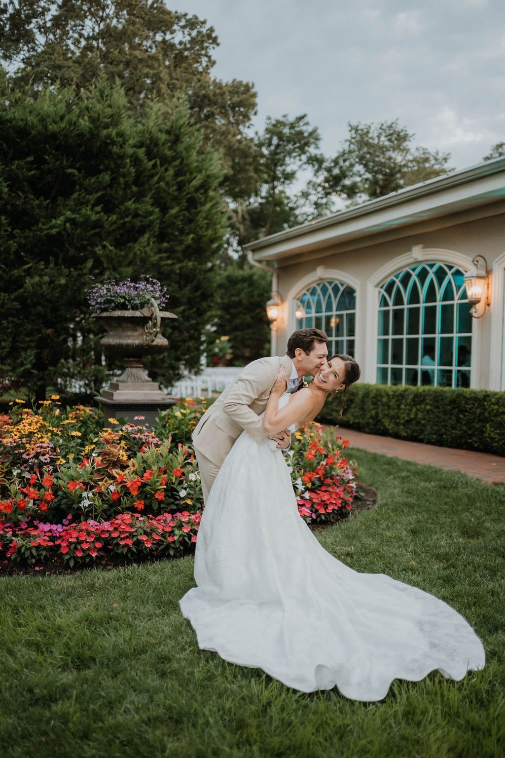 Groom dips and kisses his bride beside the garden flower bed
